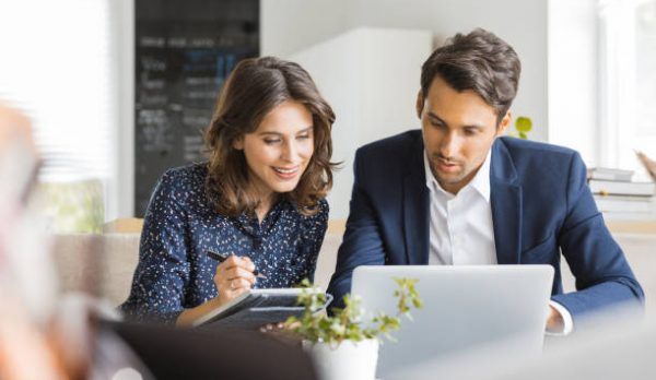 Two business people sitting at cafe working on new project using laptop. Young businesswoman taking notes and businessman working on laptop computer.